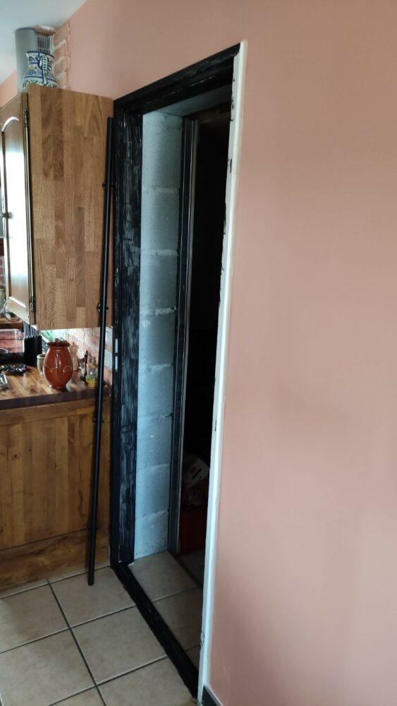 Ouverture de porte avec encadrement peint en noir et rail de porte coulissante en attente, à côté d'une cuisine en bois