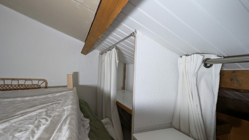 Sous-pente habillée de lambris PVC blanc, avec deux tringles et des rideaux blancs devant des rangements